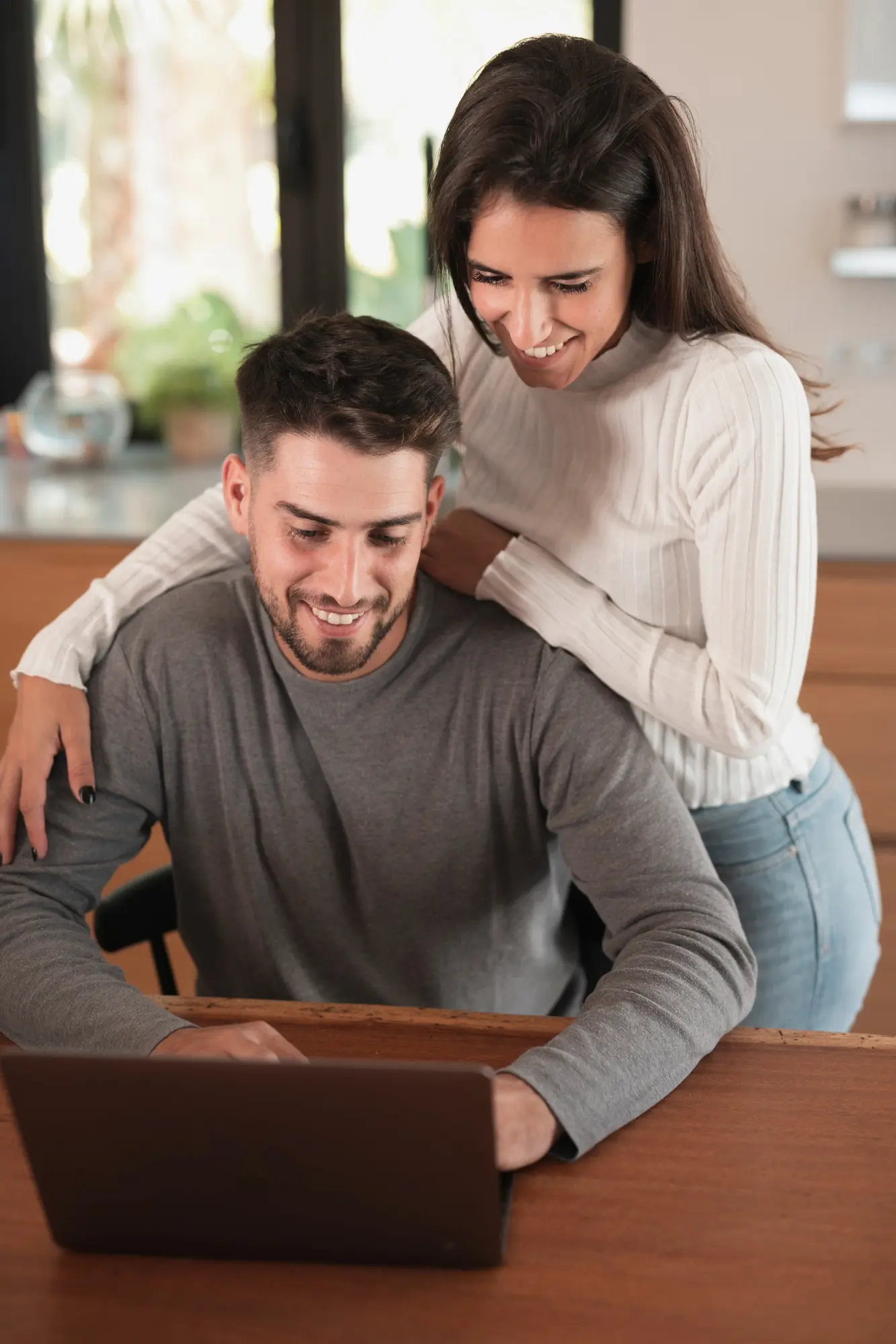 Pareja frente al portátil en la sala de su casa sonrientes por un proyecto web que soluciono un problema de alcance y visibilidad de su negocio