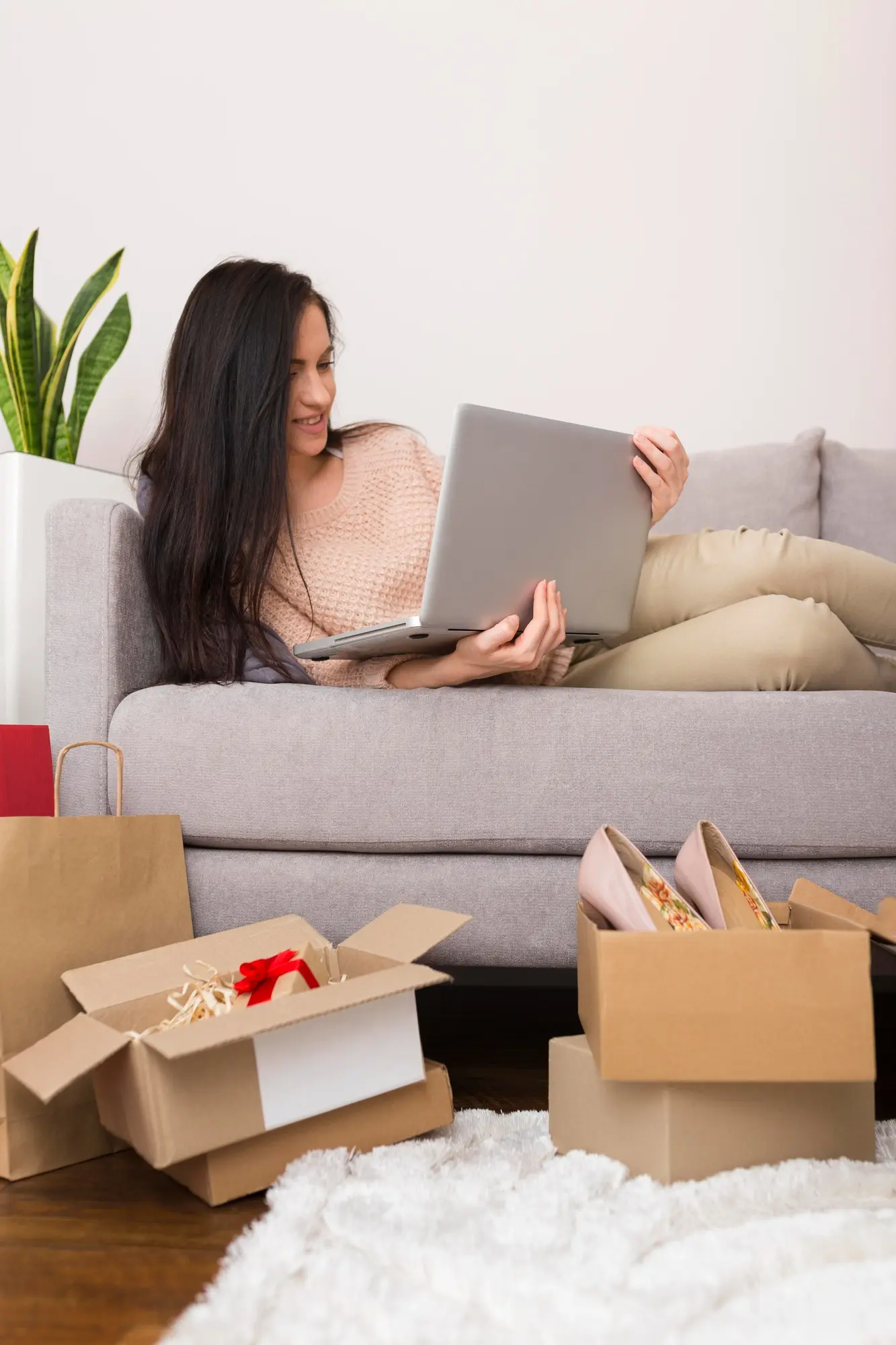 Mujer recostada en el sofa viendo en su laptop el panel de ventas y embalando productos para enviar pedidos a sus clientes, Tienda en línea desarrollada por Sodecompany