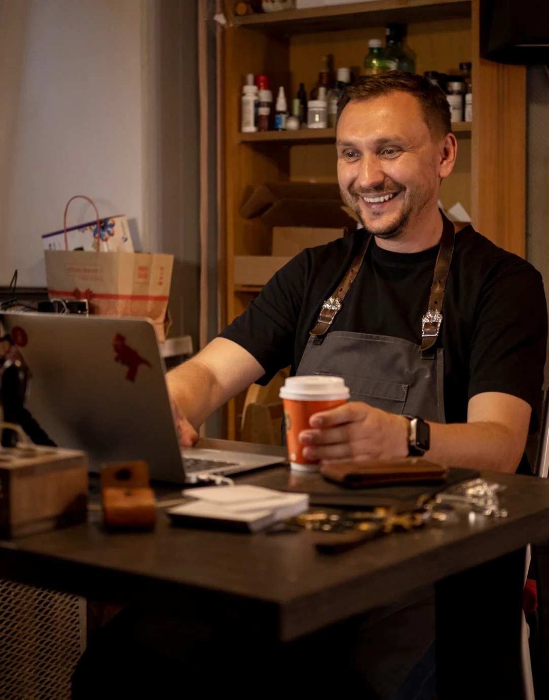 Hombre sentado en su escritorio viendo su laptop con satisfacción y tomando cafe 