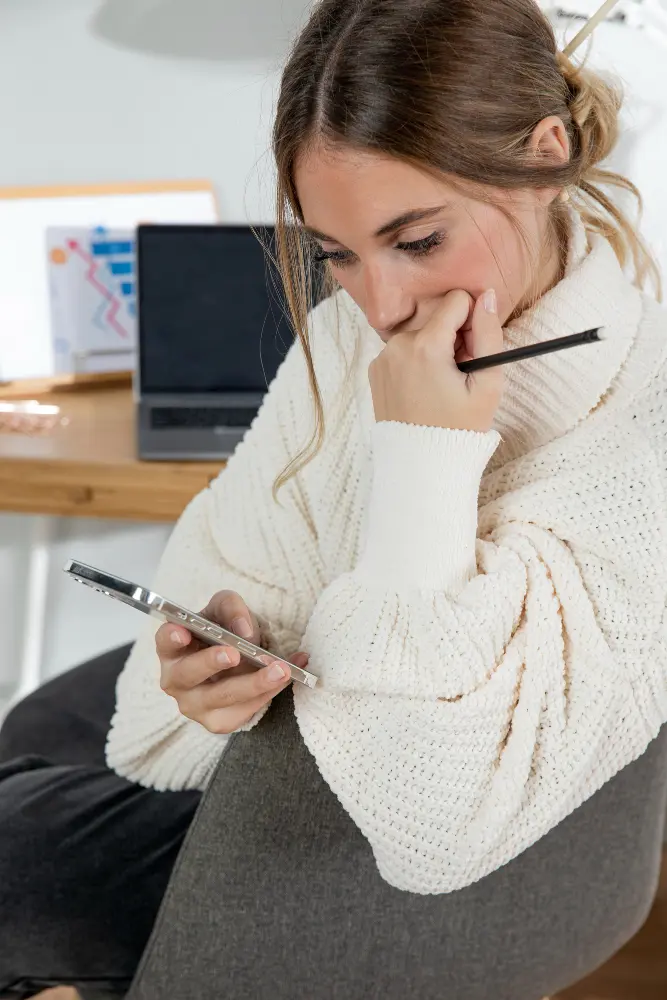 mujer dueña de negocio sentada en su escritorio viendo su teléfono con preocupación el no tener un sitio web profesional